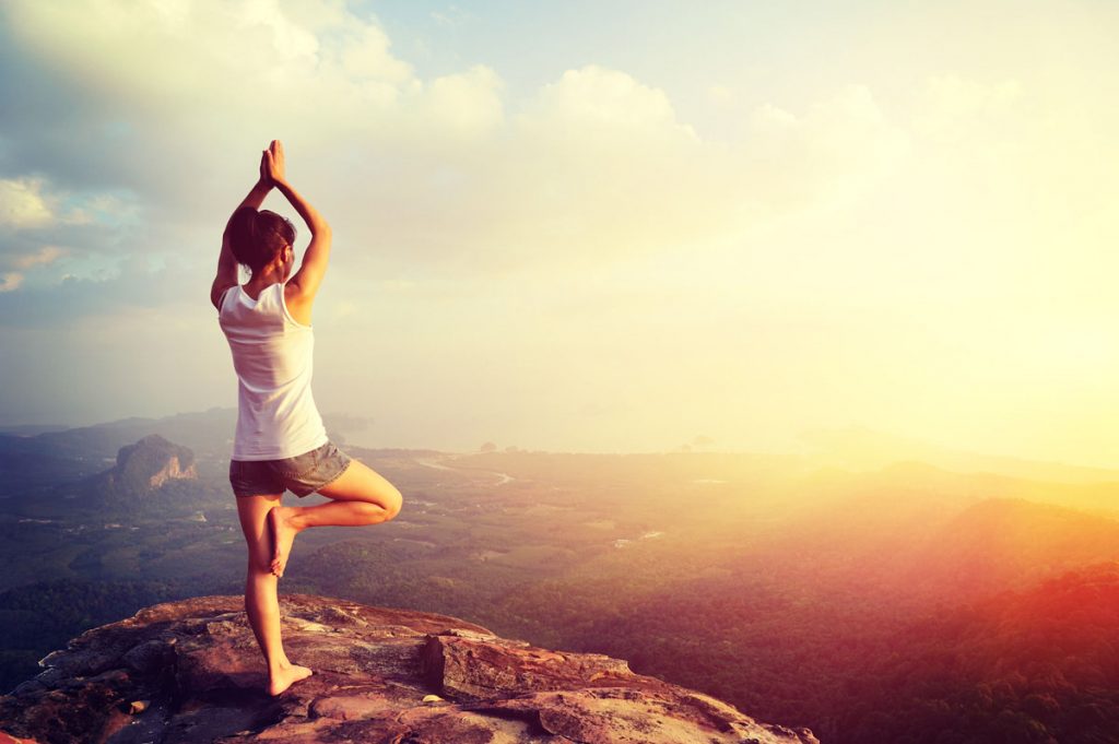 Woman doing yoga on sunny cliff